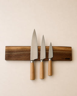 20 inch live edge walnut magnetic knife holder with three chef knives mounted on a neutral background