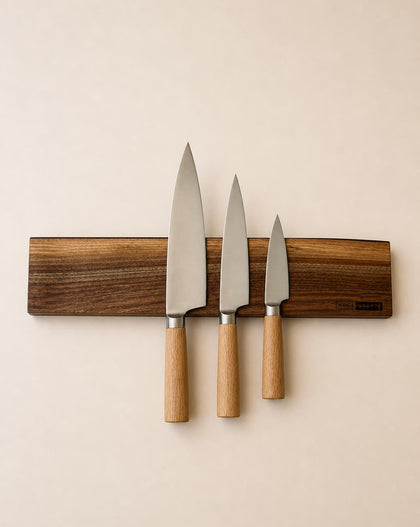 20 inch live edge walnut magnetic knife holder with three chef knives mounted on a neutral background