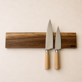20 inch live edge walnut magnetic knife holder with three chef knives mounted on a neutral background