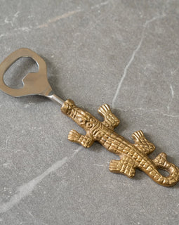 Brass alligator bottle opener with stainless steel head on gray stone background.