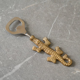 Brass alligator bottle opener with stainless steel head on gray stone background.