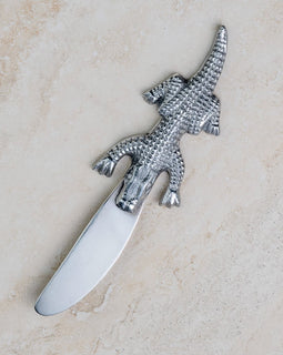 Alligator-handle stainless steel spreader on light stone background.