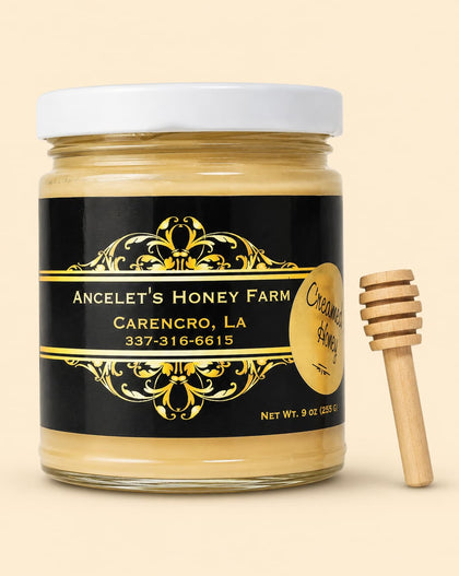 A jar of Ancelet's Honey Farm Organic Raw Honey with a black and gold label and a wooden honey dipper, set against a solid light beige background.