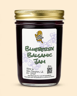 A glass jar of Blueberry Balsamic Jam with a gold metal lid and a white label featuring the 'Once Loving Kitchen' logo, set against a solid beige background.