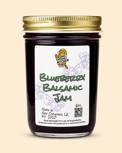 A glass jar of Blueberry Balsamic Jam with a gold metal lid and a white label featuring the 'Once Loving Kitchen' logo, set against a solid beige background.
