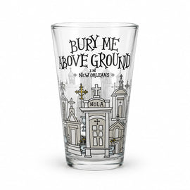 A clear pint glass featuring a black and white graphic illustration of New Orleans cemeteries and the text 'BURY ME ABOVE GROUND IN NEW ORLEANS' on a white background.
