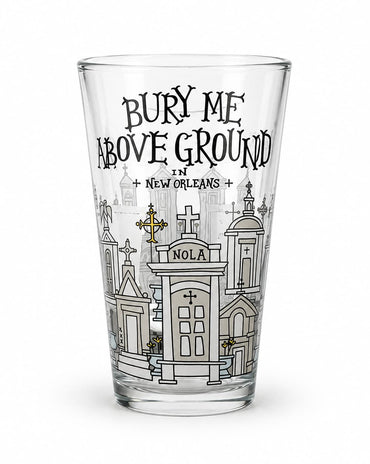 A clear pint glass featuring a black and white graphic illustration of New Orleans cemeteries and the text 'BURY ME ABOVE GROUND IN NEW ORLEANS' on a white background.