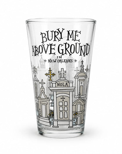 A clear pint glass featuring a black and white graphic illustration of New Orleans cemeteries and the text 'BURY ME ABOVE GROUND IN NEW ORLEANS' on a white background.