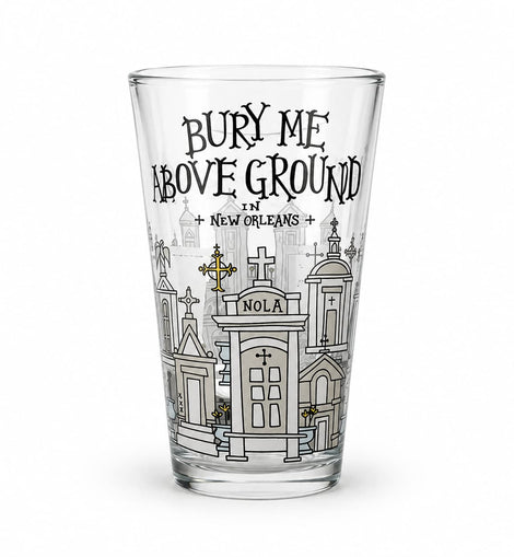 A clear pint glass featuring a black and white graphic illustration of New Orleans cemeteries and the text 'BURY ME ABOVE GROUND IN NEW ORLEANS' on a white background.