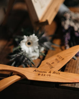 Cherry wood cake knife and server set with engraved names displayed on a rustic table with flowers.