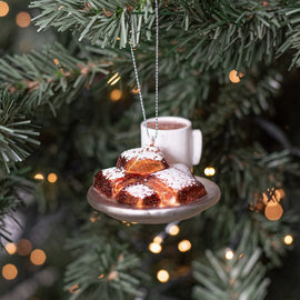 Ornament of powdered sugar beignets on a plate with a cup of coffee hanging on a Christmas tree.”