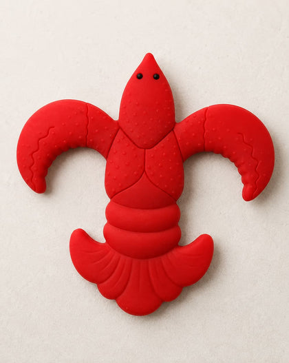 A bright red lcrawfish baby teether shown on a light beige textured background.