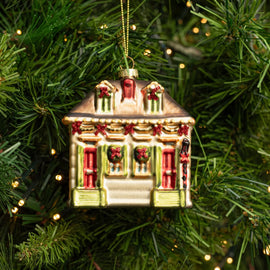 Glass Creole Cottage ornament with red doors, green shutters, and glittery holiday decorations hanging on a Christmas tree.