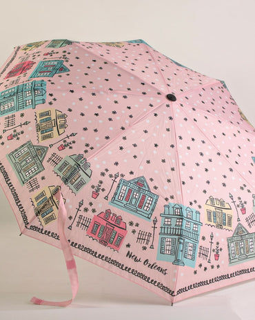 Pink travel umbrella featuring illustrated New Orleans Creole cottages and architectural homes with wrist strap displayed open.