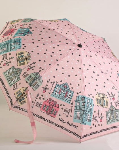 Pink travel umbrella featuring illustrated New Orleans Creole cottages and architectural homes with wrist strap displayed open.