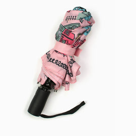 Pink travel umbrella featuring illustrated New Orleans Creole cottages and architectural homes with wrist strap displayed closed.