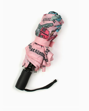 Pink travel umbrella featuring illustrated New Orleans Creole cottages and architectural homes with wrist strap displayed closed.