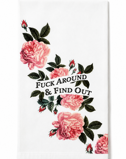 A white kitchen towel featuring a vertical arrangement of pink roses with dark green leaves and the humorous text 'FUCK AROUND & FIND OUT' in black serif lettering.