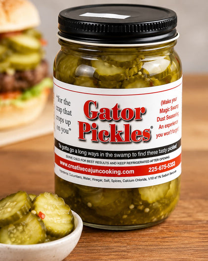 A jar of Gator Pickles with a black lid and a white label featuring red and black text, set on a wooden table with sliced pickles in a small bowl and a blurred burger in the background.