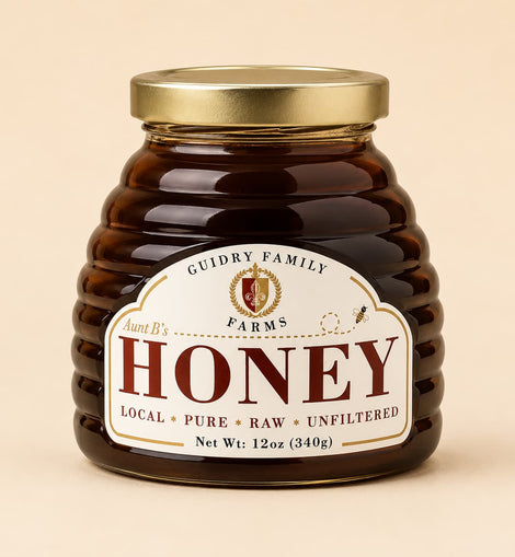 A jar of honey from Guidry Family Farms, Aunt B's, with a ribbed amber glass body, a gold metal lid, and a cream-colored label with red lettering, set against a solid beige background.