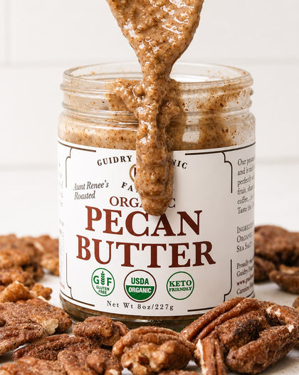 A jar of Guidry Organic Organic Pecan Butter with pecans and a spoonful of the spread dripping out, set against a white tiled background.
