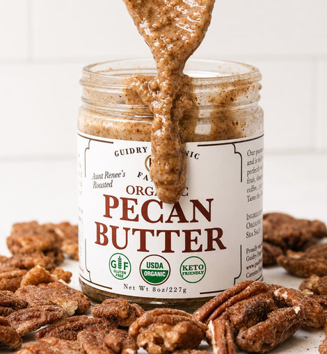 A jar of Guidry Organic Organic Pecan Butter with pecans and a spoonful of the spread dripping out, set against a white tiled background.