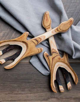Guitar-shaped wooden salad hands made from layered hardwoods, displayed on a gray cloth atop a wooden surface.