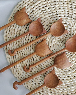 Hand-carved wooden cat stirring spoon with cat-shaped top and curved tail handle on a white background.