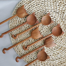 Hand-carved wooden cat stirring spoon with cat-shaped top and curved tail handle on a white background.