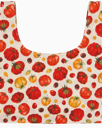 A reusable tote bag with a printed pattern of red, orange, and yellow tomatoes on an off-white background.