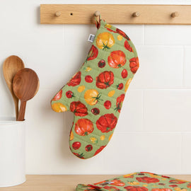 Quilted cotton oven mitt with heirloom tomato print in red and yellow tones hanging on kitchen rack with wooden utensils nearby.
