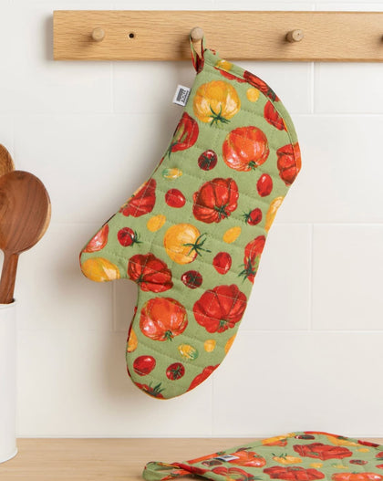 Quilted cotton oven mitt with heirloom tomato print in red and yellow tones hanging on kitchen rack with wooden utensils nearby.