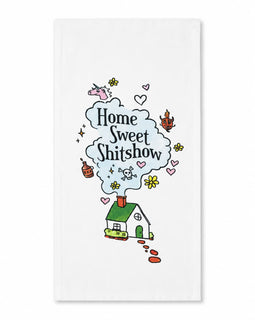A white kitchen towel featuring a whimsical cartoon illustration of a small green house with a red chimney, emitting a light blue cloud of text that reads 'Home Sweet Shitshow' in black script. The design is decorated with small pink hearts, yellow flowers, and other doodles, set against a clean white background.