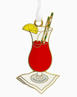 Enamel Hurricane cocktail ornament with lemon slice, cherry, striped straws, and ‘New Orleans’ napkin.