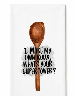 A white kitchen towel featuring a brown wooden spoon illustration and the text 'I MAKE MY OWN ROUX, WHATS YOUR SUPERPOWER?' in black lettering.