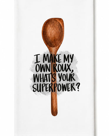 A white kitchen towel featuring a brown wooden spoon illustration and the text 'I MAKE MY OWN ROUX, WHATS YOUR SUPERPOWER?' in black lettering.