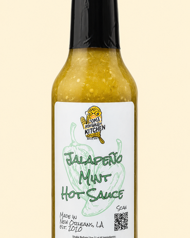A bottle of Jalapeño Mint Hot Sauce by Smokey's Kitchen, featuring a white label with green text and a black cap, set against a solid pale beige background.