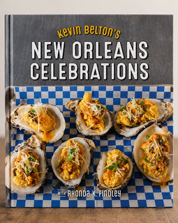 The front cover of the book 'Kevin Belton's New Orleans Celebrations' is shown standing upright on a wooden surface against a light neutral background. The cover features a dark gray upper section with the title in white and yellow text, and a lower section showing several oysters topped with yellow sauce on a blue-and-white checkered surface.