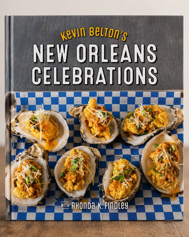 The front cover of the book 'Kevin Belton's New Orleans Celebrations' is shown standing upright on a wooden surface against a light neutral background. The cover features a dark gray upper section with the title in white and yellow text, and a lower section showing several oysters topped with yellow sauce on a blue-and-white checkered surface.
