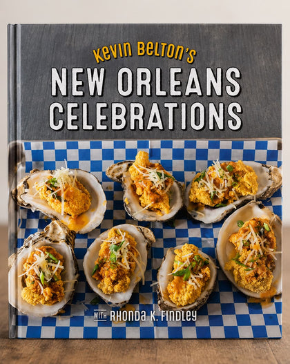 The front cover of the book 'Kevin Belton's New Orleans Celebrations' is shown standing upright on a wooden surface against a light neutral background. The cover features a dark gray upper section with the title in white and yellow text, and a lower section showing several oysters topped with yellow sauce on a blue-and-white checkered surface.