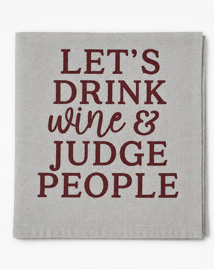 A square light gray linen napkin with the phrase 'LET'S DRINK wine & JUDGE PEOPLE' printed in dark red lettering, shown flat against a white background.