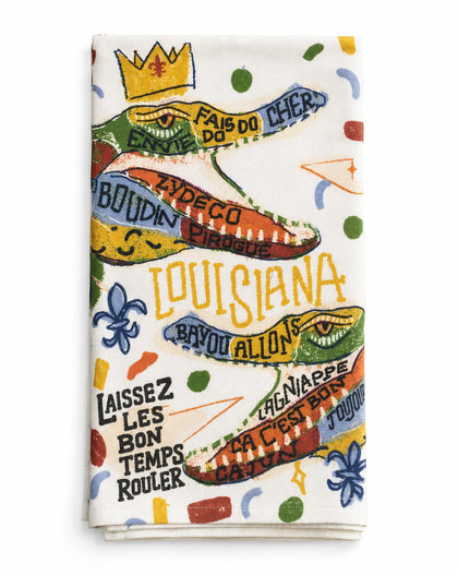 A folded white kitchen towel featuring a colorful, playful crocodile design with French Louisiana-themed text and motifs, including 'LOUISIANA' and 'FAIS DO DO CHER'.