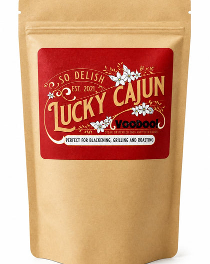 A kraft paper stand-up pouch with a large red front label reading 'So Delish Lucky Cajun' and 'Perfect for blackening, grilling and roasting.'.