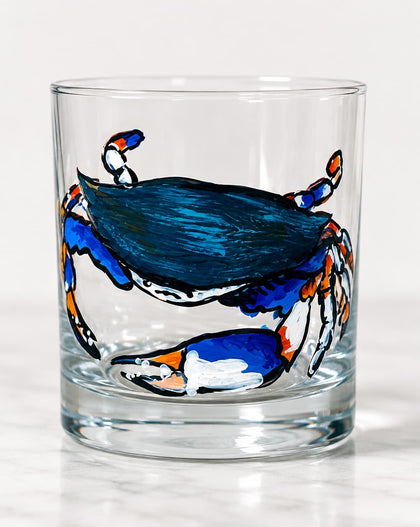 A clear glass rocks tumbler featuring a hand-painted blue crab design on the front, set against a clean white background.
