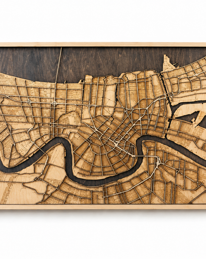 A rectangular wooden city map wall art piece featuring a laser-engraved street grid and a winding river, shown in a light wood frame against a plain white background.