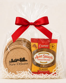 A New Orleans-themed gift basket featuring a bag of Aunt Sally's Creole Pralines and a set of cork coasters, wrapped in clear cellophane with a red ribbon and white paper shred.