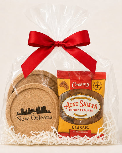 A New Orleans-themed gift basket featuring a bag of Aunt Sally's Creole Pralines and a set of cork coasters, wrapped in clear cellophane with a red ribbon and white paper shred.
