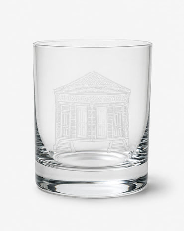 A clear glass rocks tumbler featuring an etched white line drawing of a classical building on the front, set against a plain light gray background.