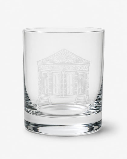 A clear glass rocks tumbler featuring an etched white line drawing of a classical building on the front, set against a plain light gray background.