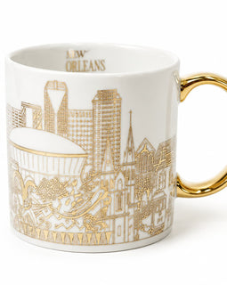 A white ceramic coffee mug featuring a gold line-art illustration of the New Orleans skyline and the word 'NEW ORLEANS' printed inside the rim, with a polished gold handle.